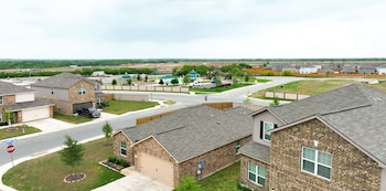 Vista aérea de un barrio residencial con casas de ladrillo, calles asfaltadas, un área recreativa infantil y terrenos despejados al fondo