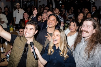 Anthony Gross (izquierda) y Kate DePetro (centro) graban un video con amigos durante un evento social en el Pizza Box de Greenwich Village, antes de la misa católica en la iglesia de San José en Nueva York, el 22 de marzo