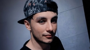 Primer plano de Ramiro Nast, un joven con gorra estampada de palmeras y camiseta negra, mirando directamente a la cámara