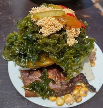 Plato de Chiriuchu con cuy asado, maíz, algas marinas verdes, granos pequeños, queso blanco, y rodajas de encurtidos y pimiento rojo, sobre una mesa oscura