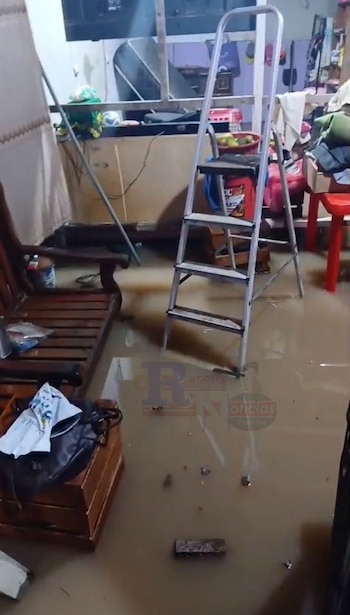 Interior de una vivienda inundada con agua lodosa cubriendo el suelo. Se ven una escalera de mano plateada y un banco de madera parcialmente sumergidos