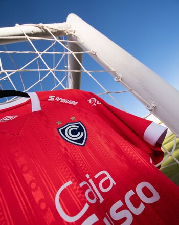 Camiseta roja del equipo de fútbol Cienciano colgada en la red y el poste de una portería contra un cielo azul