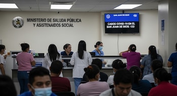 Personas en la recepción del Ministerio de Salud Pública y Asistencia Social. Un monitor muestra 'Casos COVID-19 en el San Juan de Dios: 132'.