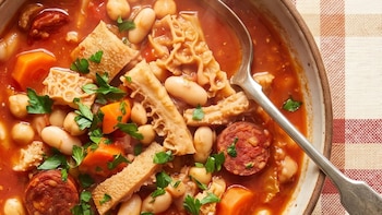 Cuenco de cerámica con guiso de mondongo, porotos, garbanzos, zanahoria, rodajas de chorizo y perejil. Una cuchara metálica reposa en el plato