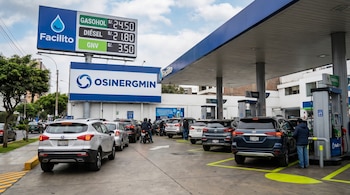 Estación de servicio urbana en Lima con autos y motos en fila. Un letrero digital muestra precios de gasohol, diésel y GNV. Logos de OSINERGMIN y Facilito son visibles.
