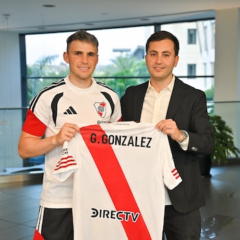 Dos hombres de pie, uno con camiseta de fútbol de River Plate, el otro de traje, sostienen una camiseta blanca con franja roja que dice G. GONZALEZ y DIRECTV