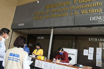 Fachada de la Oficina de Atención a la Víctima del Ministerio Público de Guatemala. Personas con mascarillas interactúan en un mostrador de recepción con carteles