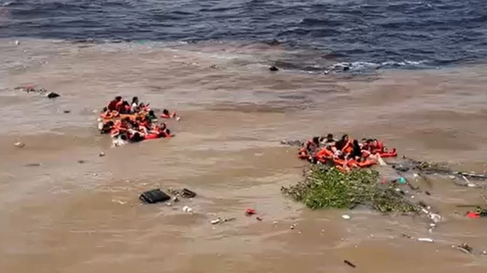 Varias personas con chalecos salvavidas flotan en dos grupos sobre aguas marrones y turbias mezcladas con desechos, mientras otras se encuentran en aguas más oscuras tras un naufragio en Brasil (Redes sociales)