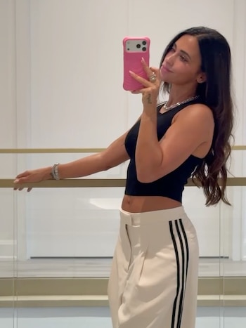 Antonela Roccuzzo se toma una autofoto frente a un espejo con un teléfono rosado, vestida con un top negro y un pantalón blanco