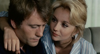 Primer plano de una mujer rubia con camisa a rayas, abrazando a un hombre de cabello castaño que mira hacia abajo, ambos en una pose cercana