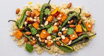 Quinoa cocida, cubos de calabaza anaranjada asada, chiles poblanos verdes chamuscados y almendras tostadas enteras y troceadas, sobre fondo claro.