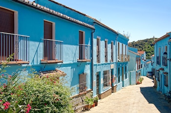 Una calle empedrada flanqueada por casas de fachada azul con persianas marrones, balcones de hierro y plantas con flores