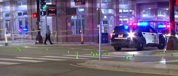 Una patrulla de policía de Minneapolis con luces azules y rojas, cinta amarilla, conos de evidencia verdes, un peatón y un edificio de ladrillo