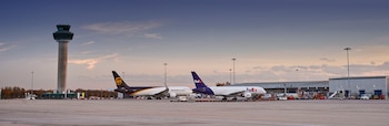 Dos aviones de carga estacionados en la pista de un aeropuerto junto a una torre de control y varios edificios