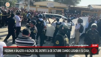 Policías y personal de serenazgo, junto a una multitud, rodean un coche oscuro en una calle; algunos sostienen una sábana blanca ocultando la escena