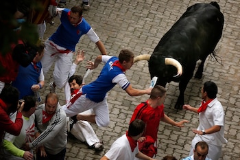 El corredor estadounidense Bill Hillmann, de 35 años y originario de Chicago, en el centro izquierda, cae segundos antes de que un toro de lidia de la hacienda Victoriano del Río lo cornee en la pierna derecha durante el encierro de las fiestas de San Fermín, en Pamplona, España, el miércoles 9 de julio de 2014. (Foto AP/Daniel Ochoa de Olza, Archivo)