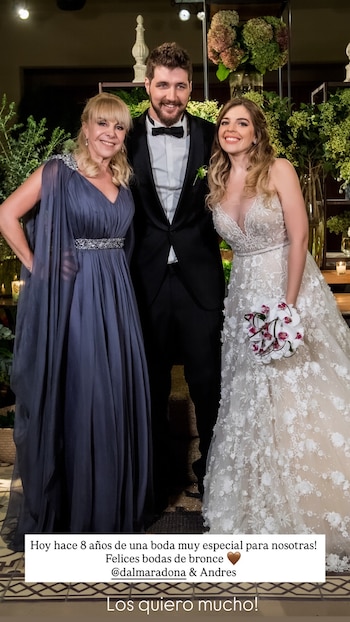 Dalma Maradona con un vestido de novia blanco, su esposo Andrés en esmoquin y una mujer en vestido azul posan sonrientes en un evento