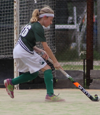 Un jugador de hockey sobre césped, Luciano Curcio, vestido con uniforme verde y blanco con el número 16, sostiene un palo Grays en la cancha