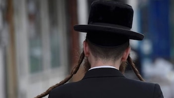 Vista trasera de un hombre judío ortodoxo con sombrero negro y traje oscuro, mostrando peyot trenzados a los lados de su cabeza