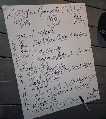 Una hoja de papel blanco con escritura a mano en negro muestra una lista numerada de nombres de artistas de hip-hop y títulos de canciones, con un rotulador negro al lado