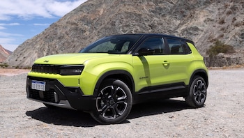 Un automóvil de color verde lima y techo negro, estacionado sobre un suelo de grava frente a montañas rocosas