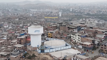 Vista aérea de una torre de agua blanca y un reservorio circular con el logotipo de Sedapal rodeados por viviendas en una ladera urbana