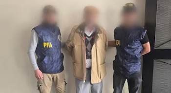 Tres personas de pie con el rostro difuminado, dos con chalecos de la Policía Federal Argentina y un hombre al centro con chaqueta beige