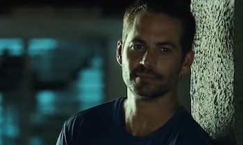 Un hombre de cabello corto y barba ligera vistiendo una camiseta azul apoya su hombro contra una columna rugosa