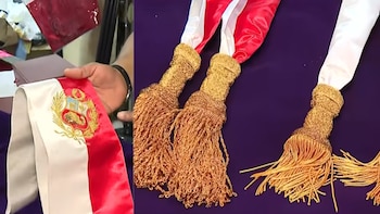 Una persona sostiene una banda presidencial bicolor con el escudo de Perú bordado; otras bandas con borlas doradas se exhiben sobre tela morada