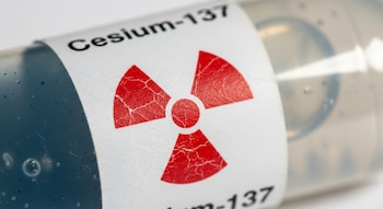 Primer plano de una cápsula de Cesio-137 con etiqueta blanca que muestra un símbolo de radiactividad rojo y el texto "Cesium-137", revelando textura rugosa y gel interno.