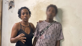 Una mujer con camiseta negra coloca su mano sobre la espalda de un joven con el rostro difuminado.