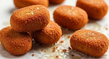 Primer plano de varias croquetas doradas y crujientes sobre papel absorbente, con pequeñas gotas de aceite visibles alrededor.