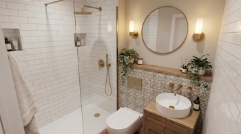 Vista interior de un baño moderno con ducha de cristal, inodoro blanco, lavabo redondo con grifería dorada, espejo circular y azulejos decorativos con plantas.