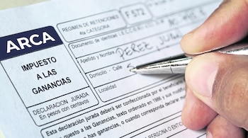 Primer plano de una mano con un bolígrafo escribiendo en un formulario blanco y azul de ARCA Impuesto a las Ganancias.