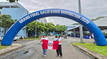 Dos mujeres sostienen la bandera peruana bajo un gran arco azul inflable con letras blancas en una vía al aire libre.