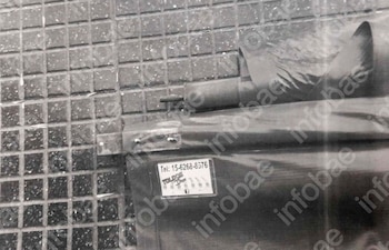 Vista cercana de un toldo oscuro y enrollado, con una etiqueta de número telefónico, tirado sobre un suelo de baldosas cuadradas grises