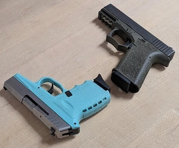Dos pistolas, una celeste y gris y otra verde oscuro con negro, colocadas sobre una superficie de madera