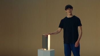 Un hombre con camiseta negra apoya su mano sobre un dispositivo rectangular iluminado ubicado encima de una base blanca