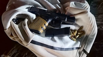 Una pistola negra con empuñadura beige, un cargador y varias balas de metal apoyadas sobre una campera blanca