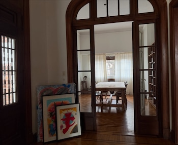 Cuadros apoyados en el suelo junto a una puerta de madera que conecta con un comedor con mesa, sillas y ventanas con cortinas