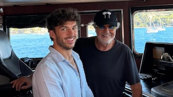 Pierre Gasly con camisa clara y Flavio Briatore con gorra y gafas de sol posan en el interior de una embarcación frente al mar