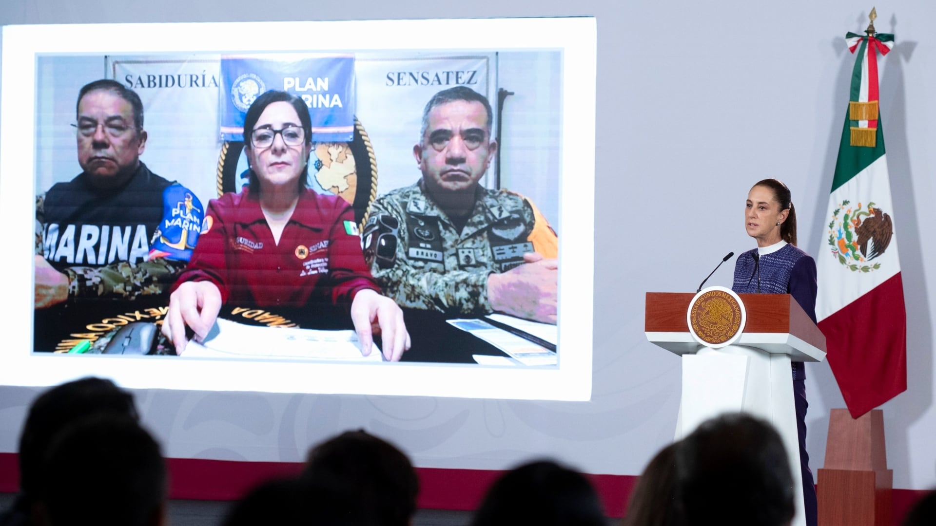 La presidenta Claudia Sheinbaum encabeza una conferencia junto a una pantalla que proyecta a funcionarios de la Coordinación Nacional de Protección Civil y la Secretaría de Marina.