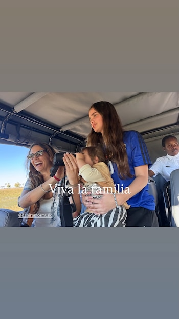 Tres personas en un vehículo de safari; una mujer con gafas de sol ríe y sostiene binoculares, un niño mira por binoculares, y una mujer abraza al niño. Un hombre se ve detrás