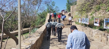 Vista trasera de tres agentes de la Guardia Nacional caminando por una senda de piedra. Al fondo, turistas suben unas escaleras de piedra entre vegetación