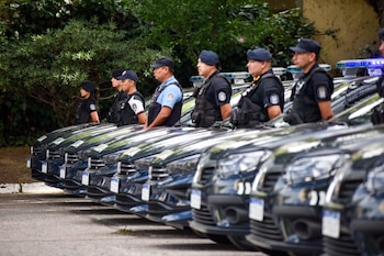 Fila de oficiales de la Policía de Buenos Aires uniformados de pie junto a seis patrulleros oscuros con luces de emergencia azules encendidas