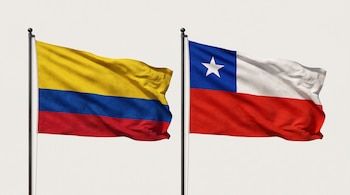 Las banderas de Colombia y de Chile flamean instaladas en dos astas oscuras sobre un fondo claro.