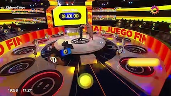 Plano general de un estudio de televisión circular donde dos hombres se saludan frente a una pantalla con la cifra de 9.600.000 pesos