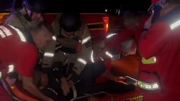 Varias personas con uniformes de rescate y chalecos reflectantes colocan a una persona sobre una camilla durante la noche