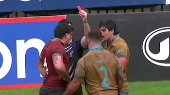 Un árbitro levanta una tarjeta roja frente a varios jugadores de rugby con camisetas rojas y amarillas