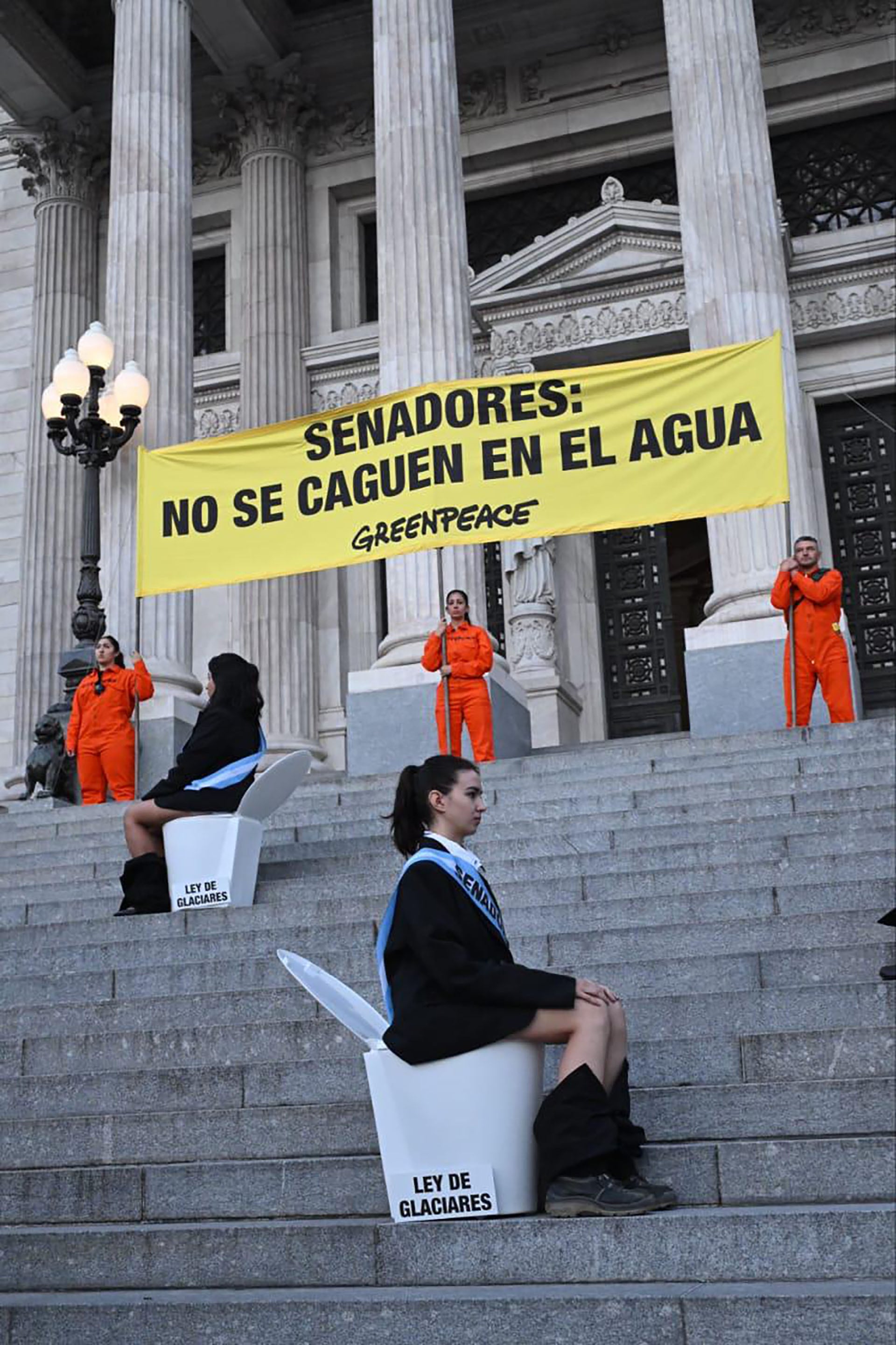 Activistas de Greenpeace protestan frente a un edificio gubernamental, instando a los senadores a proteger el agua y la Ley de Glaciares, utilizando carteles y símbolos de inodoros. (.)